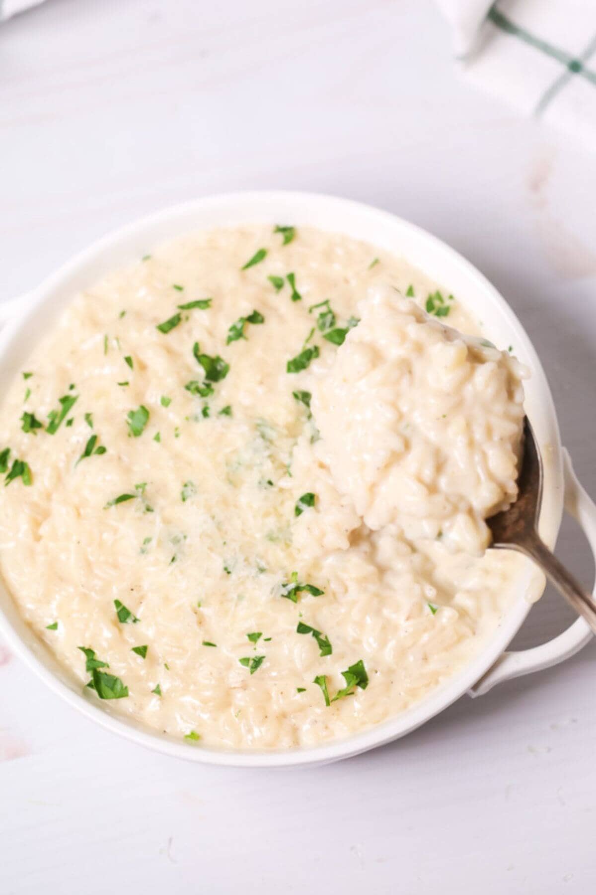 A bowl of creamy side dish topped with chopped parsley, with a spoon elegantly lifting a portion from the side.