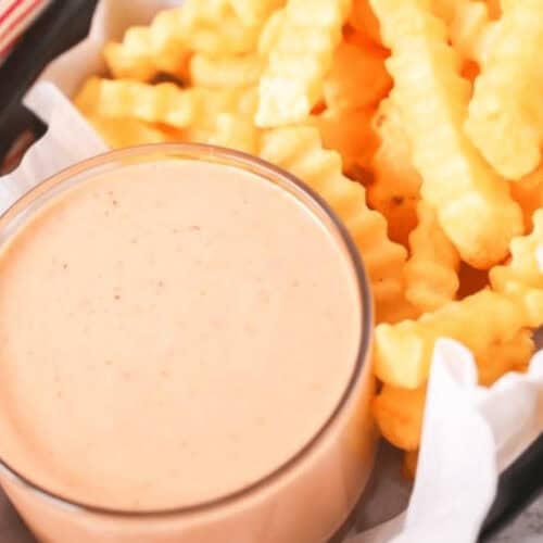 Crinkle-cut fries served with a creamy fry sauce, all nestled in a black tray lined with parchment paper.