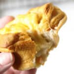 A close-up of a hand holding a torn Chicken Pot Pie Grands Biscuit with melted cheese stretching between the two halves.