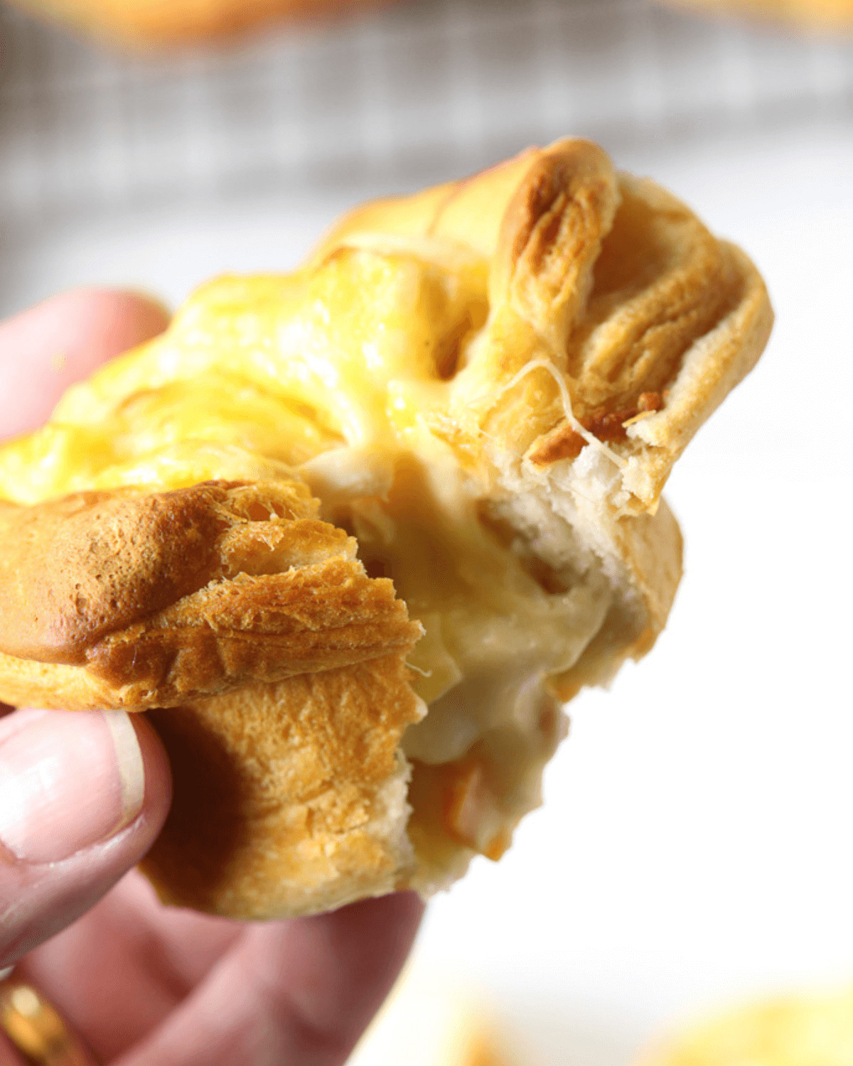 A close-up of a hand holding a torn Chicken Pot Pie Grands Biscuit with melted cheese stretching between the two halves.