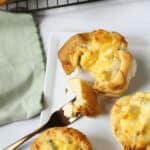 Freshly baked chicken pot pie Grands biscuits on a white plate with one being cut into, cooling on a wire rack beside a green napkin.