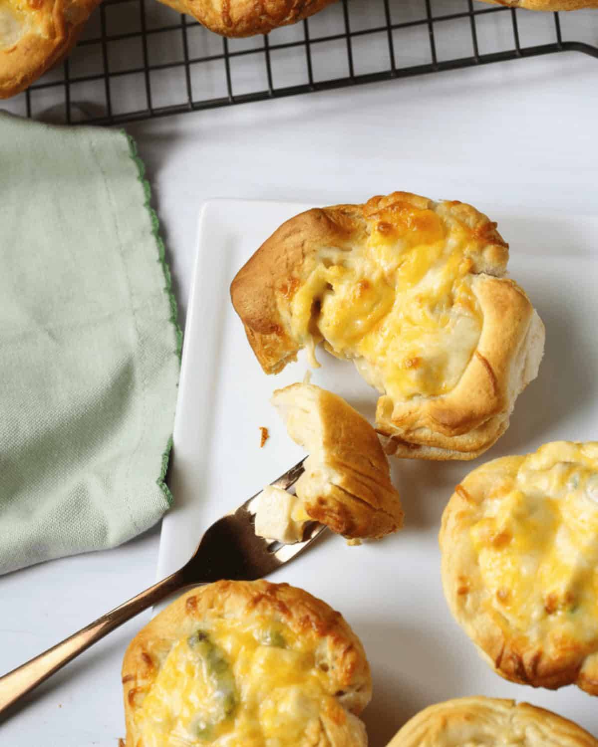 Freshly baked chicken pot pie Grands biscuits on a white plate with one being cut into, cooling on a wire rack beside a green napkin.