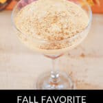A Pumpkin Spice White Russian cocktail elegantly served in a glass, crowned with a dusting of cinnamon, sits gracefully before the backdrop of vibrant autumn leaves.