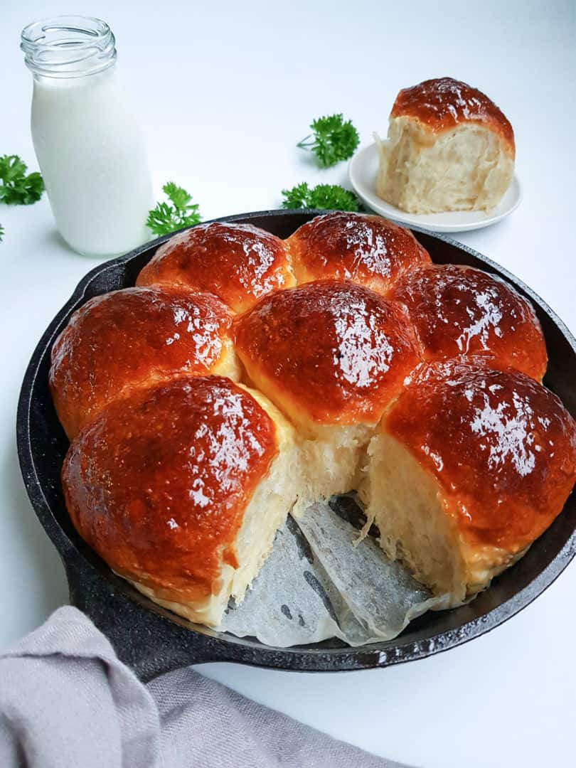 Easy homemade dinner rolls in a cast iron skillet with one roll removed and placed to the side and a glass of milk