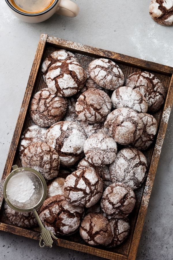 Easy brownie crinkle cookies on a wooden tray with a sifter of powdered sugar