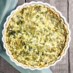 Freshly baked ham and cheese spinach quiche on a wooden table.