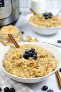 Instant Pot Maple and Brown sugarOatmeal in a white bowl with a cinnamon stick and blueberries