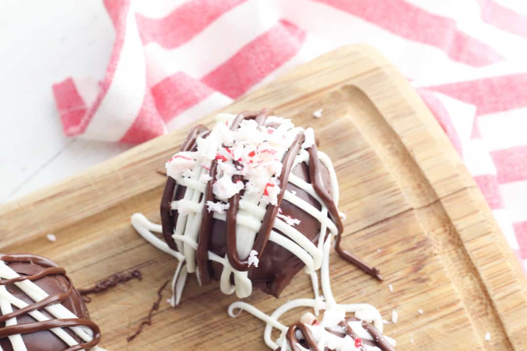 Peppermint hot cocoa bombs on a wooden cutting board with a red plaid napkin on the side. 