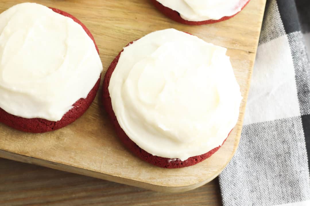 REd velvet cookies with vanilla frosting on a wood cutting board