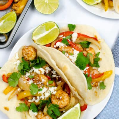 Sheet Pan Shrimp Fajitas in taco shells with slices of lime