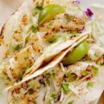 Tilapia fish tacos in crispy shells with lime wedges