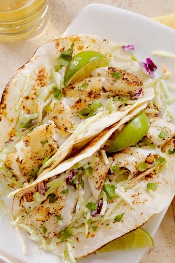 Tilapia fish tacos in crispy shells with lime wedges