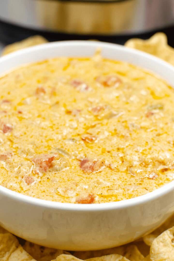A crock pot queso dip with creamy texture, featuring visible chunks of tomato and spices, surrounded by tortilla chips.