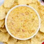 A bowl of creamy Crock Pot Queso Dip is surrounded by tortilla chips on a white plate.