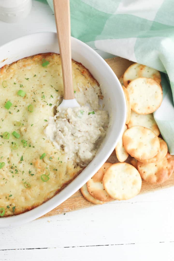 Baked crab dip recipe in a baking dish with crackers and a spatula