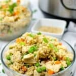 A glass bowl filled with instant pot chicken fried rice featuring peas, carrots, and green onions, with an Instant Pot and another bowl of rice in the background.