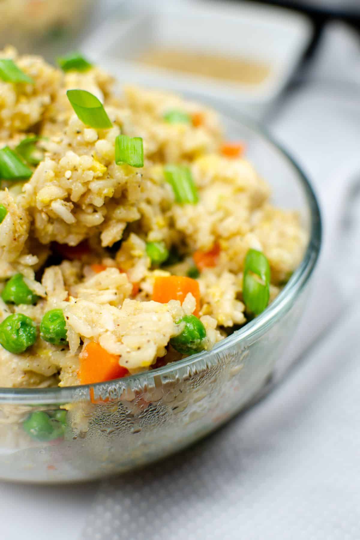 A glass bowl filled with flavorful featuring peas, carrots, and green onions.