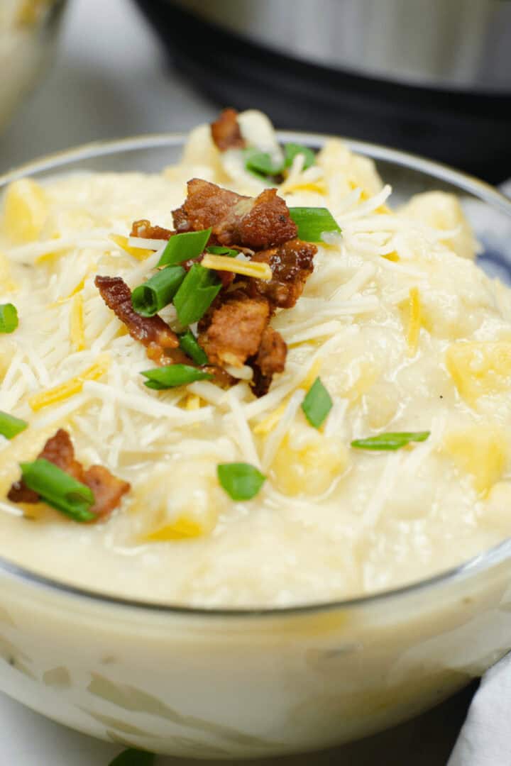 A bowl of creamy Instant Pot Loaded Potato Soup topped with crumbled bacon, shredded cheese, and chopped green onions.