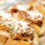 Close-up of a meatball subs recipe, showcasing delicious subs topped with marinara sauce and grated cheese on a wooden board.