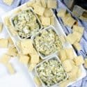 Three white bowls of Spinach artichoke dip surrounded by crackers