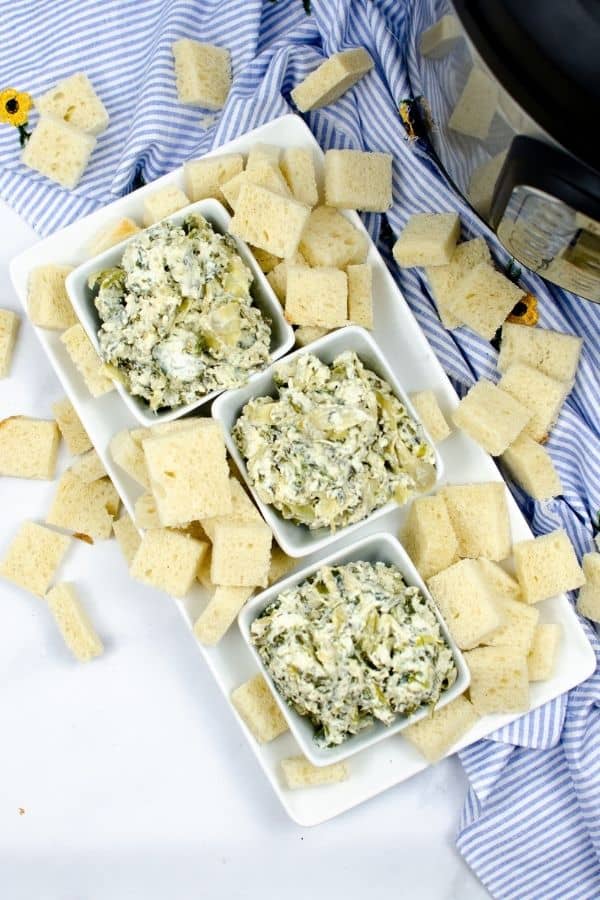 Three white bowls of Spinach artichoke dip surrounded by crackers