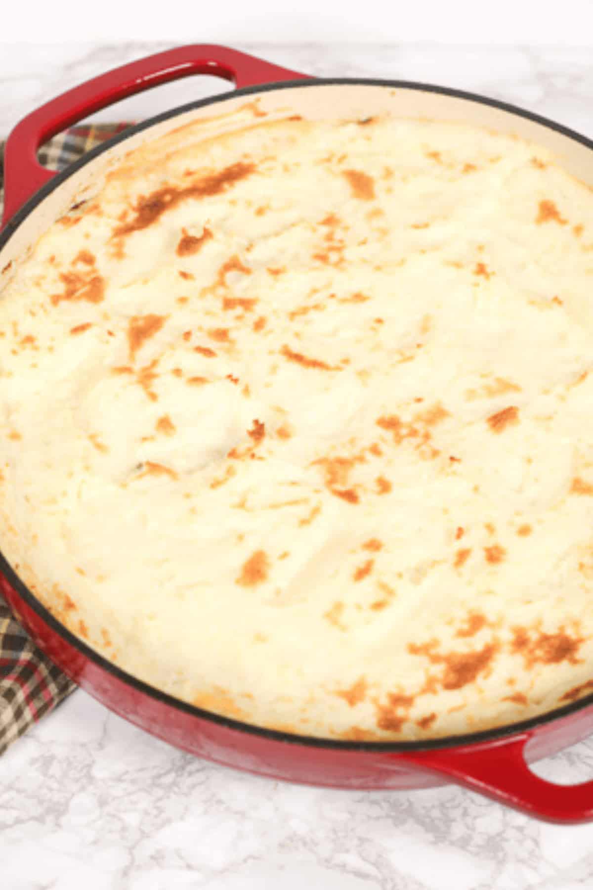 Ground beef, featuring a golden mashed potato topping in a red skillet on a marble surface.