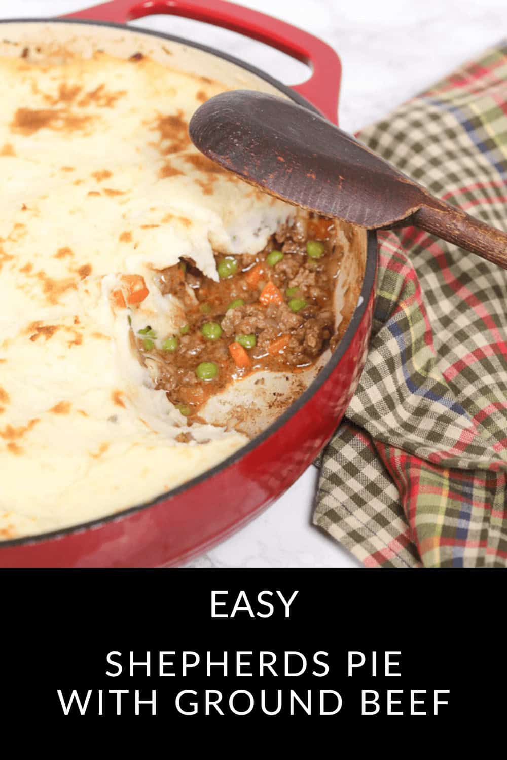 A red dish displays a delicious shepherd's pie with a portion removed, showcasing the recipe's ground beef, peas, and carrots nestled under a layer of mashed potatoes. A wooden spoon rests invitingly on the dish.