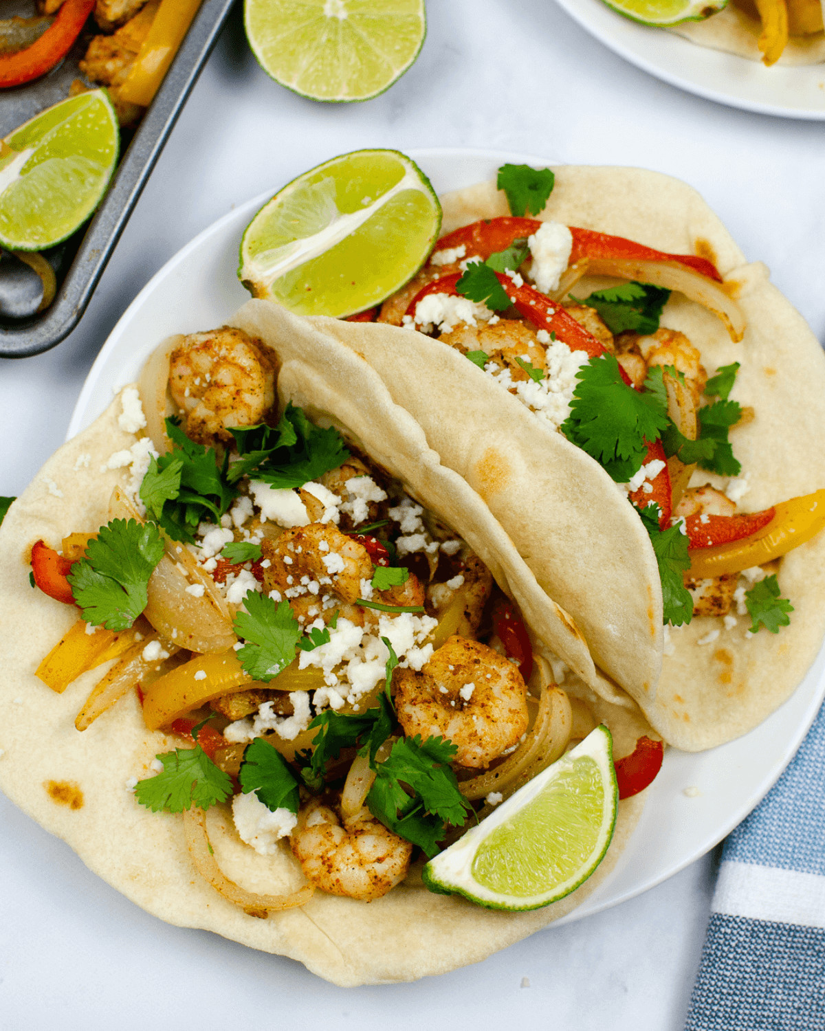 Two shrimp fajitas with bell peppers, cilantro, and lime wedges on a white plate, shot from above.