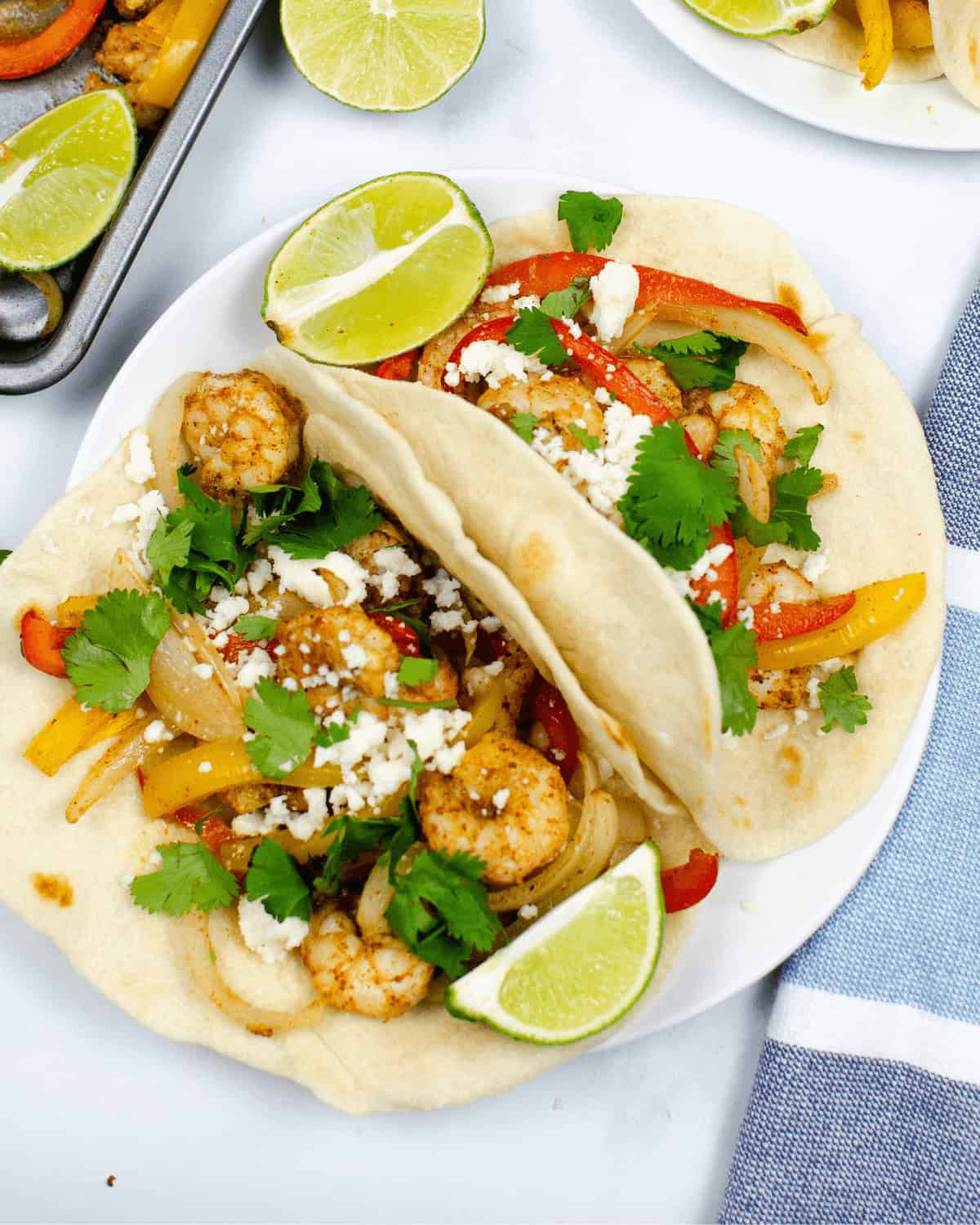 Colorful bell peppers, crumbled cheese, cilantro, and lime wedges on a white plate, close-up.