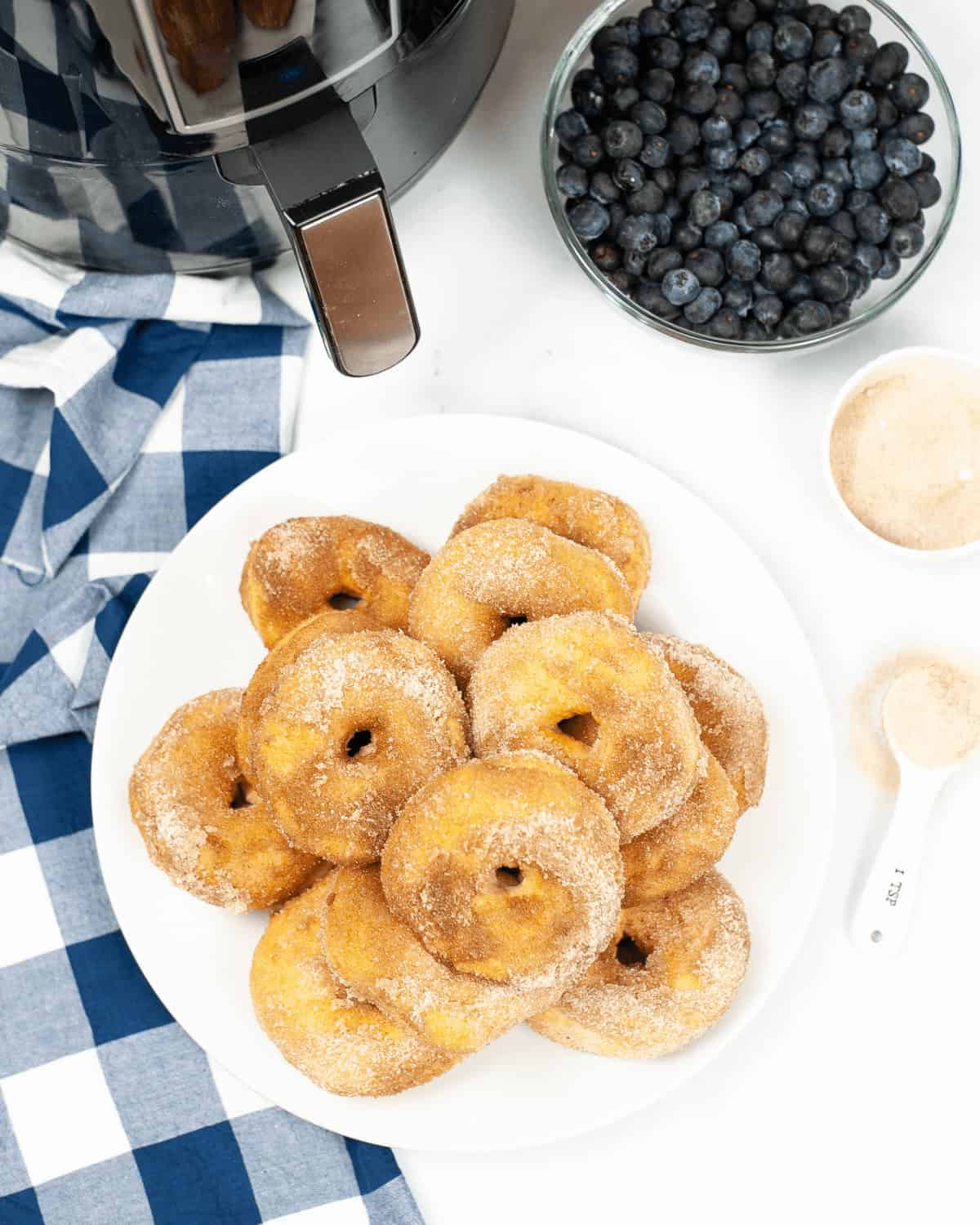 A plate of dessert on a blue and white checkered napkin, with blueberries, a sugar bowl, and a coffee pot nearby.
