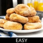 Plate of sugar-coated Air Fryer Biscuit Donuts, with a pitcher of orange juice and a blue striped cloth in the background.