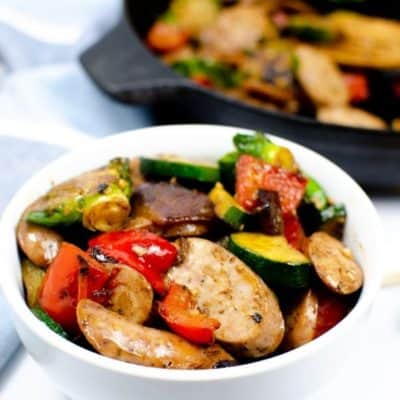 White bowl of Chicken Apple Sausage and vegetables with skillet in background