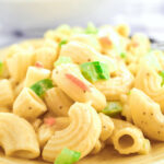 A Hellman's creamy classic macaroni salad with egg, green bell peppers and bits of red pepper on a yellow plate.