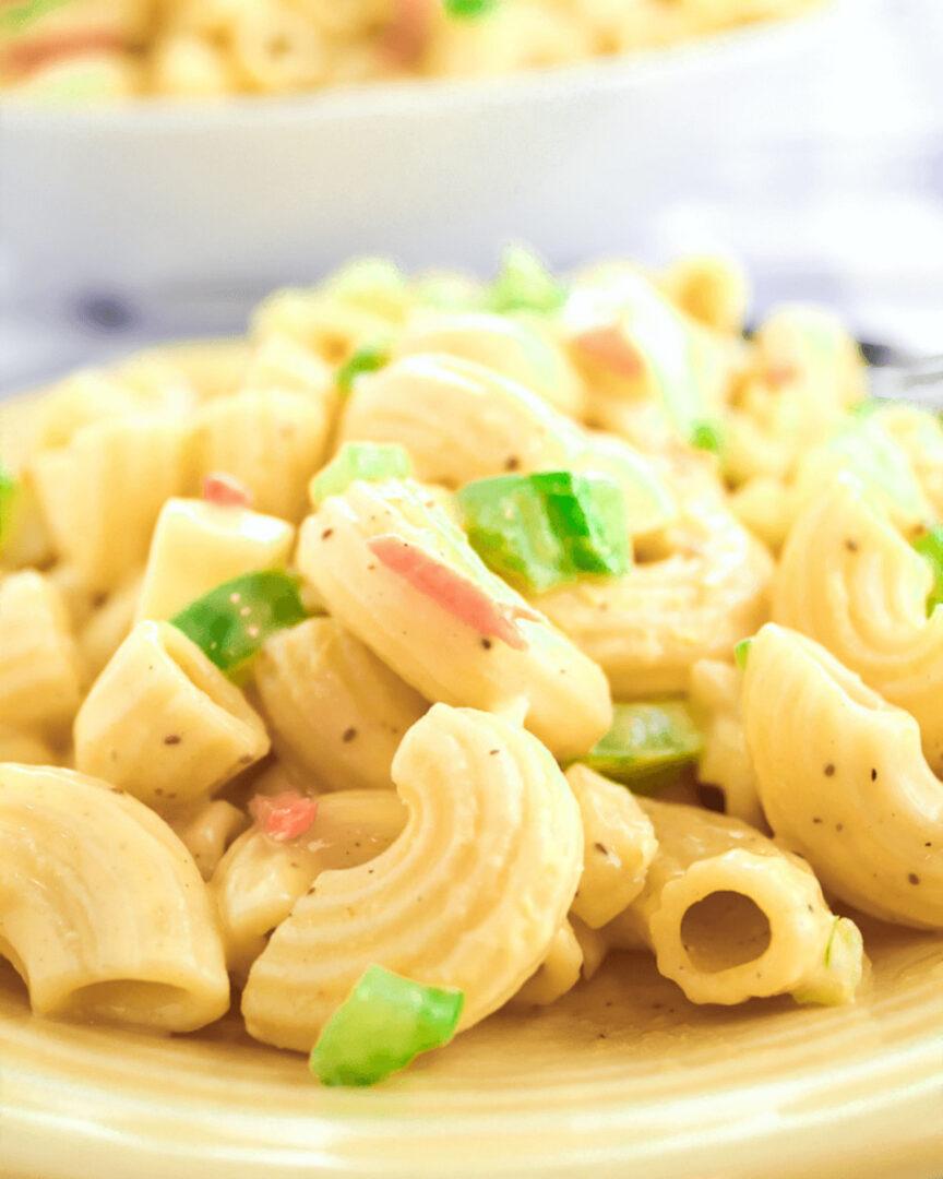 A Hellman's creamy classic macaroni salad with egg, green bell peppers and bits of red pepper on a yellow plate.