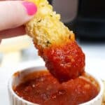 A hand dipped in marinara sauce, with a white ramekin of sauce visible below.