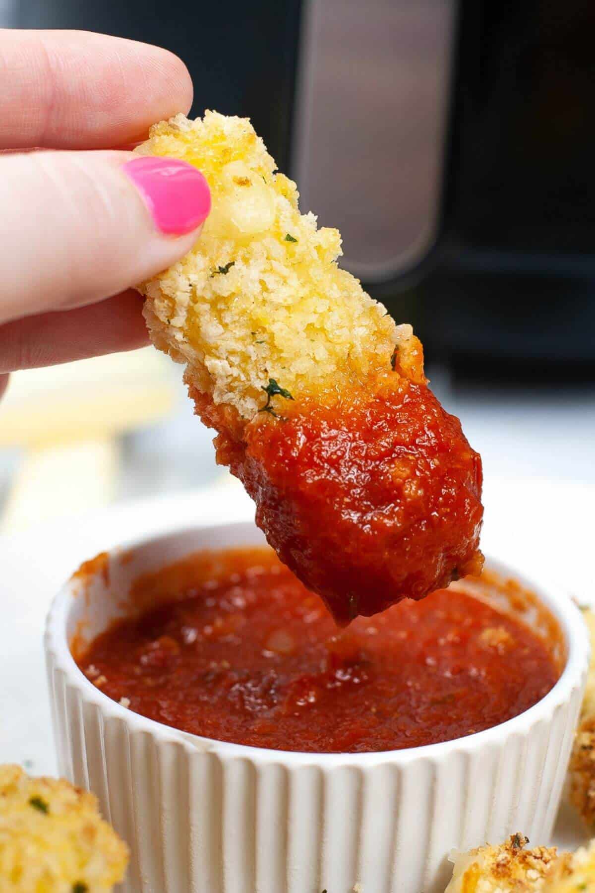 A hand dipped in marinara sauce, with a white ramekin of sauce visible below.