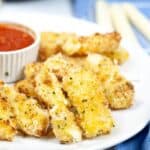 A plate of cheese appetizer garnished with herbs, served with a small cup of marinara sauce.