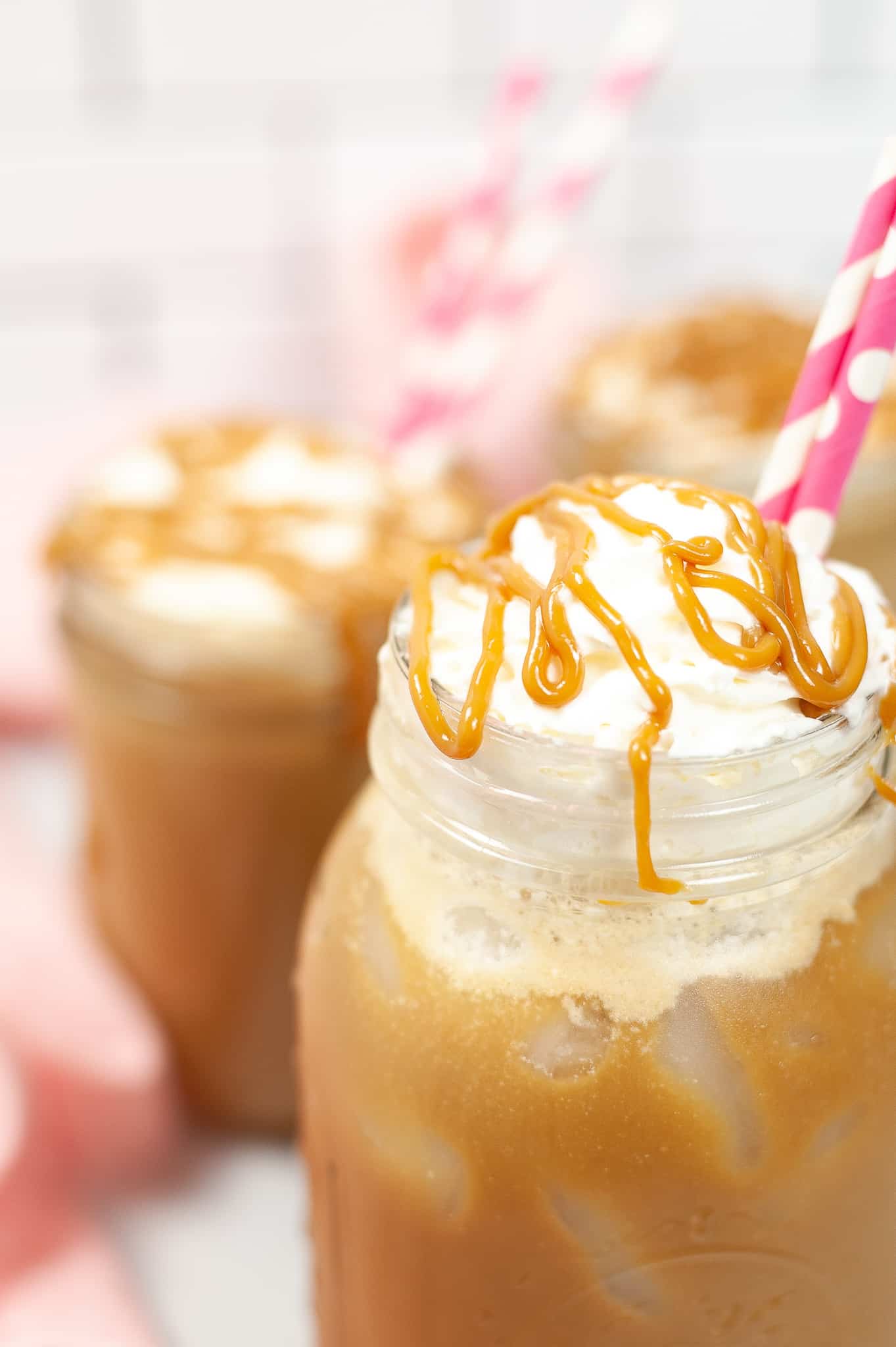 Close up of Iced caramel macchiato in a mason jar with a pink straw and caramel drizzle on top