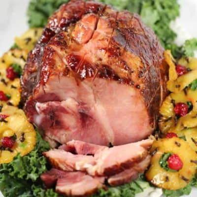 Pineapple Glazed Ham shot from the top on a white dish surrounded by pineapple and greens