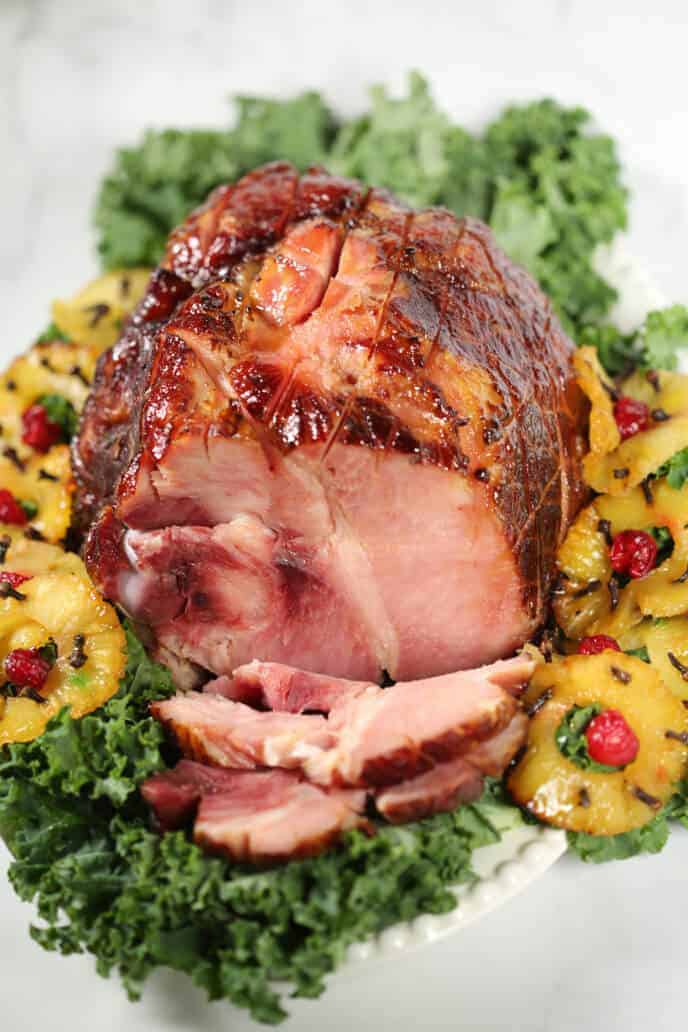 Pineapple Glazed Ham shot from the top on a white dish surrounded by pineapple and greens