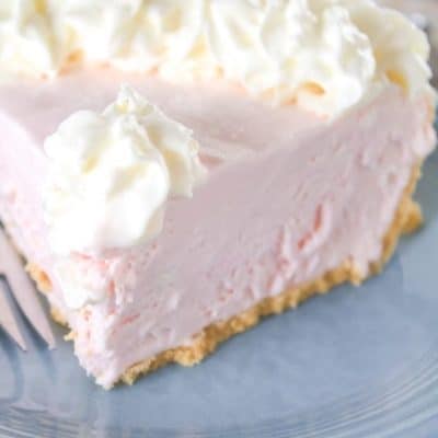 Slice of pink lemonade pie on a blue plate with a fork.