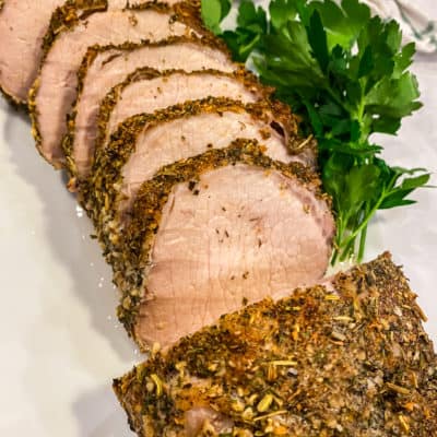 A sliced porchetta with greens on side