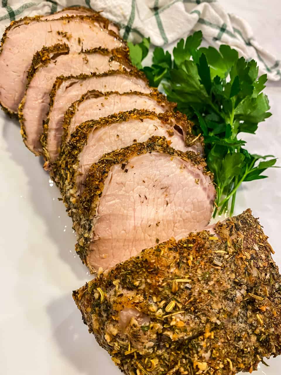 A sliced porchetta with greens on side