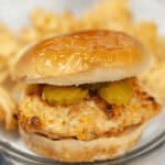 A copycat Chick Fil A sandwich with pickles is served on a plate alongside crispy waffle fries.
