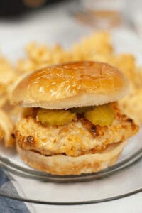 A copycat Chick Fil A sandwich with pickles is served on a plate alongside crispy waffle fries.