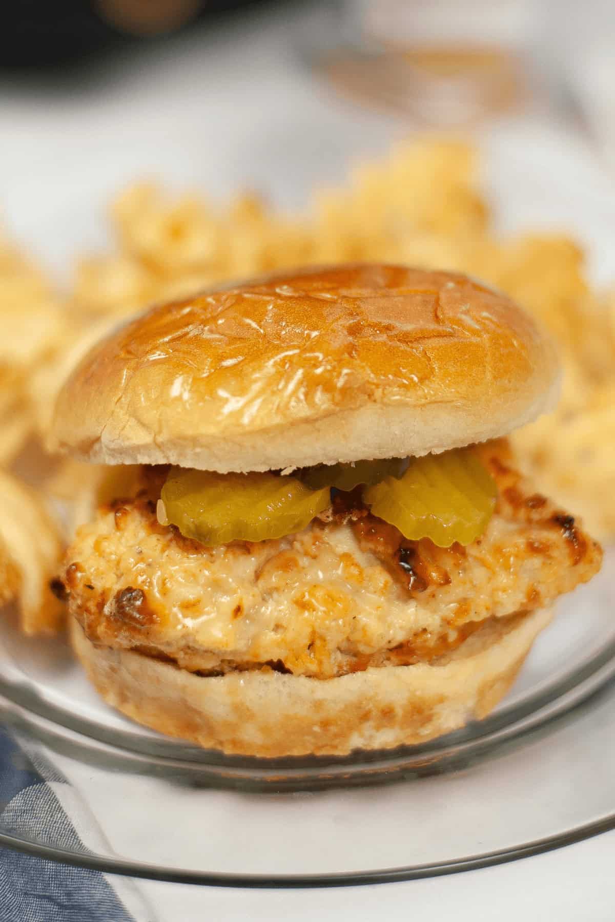 A copycat Chick Fil A sandwich with pickles is served on a plate alongside crispy waffle fries.