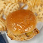 A roll with chicken on a plate surrounded by waffle fries.