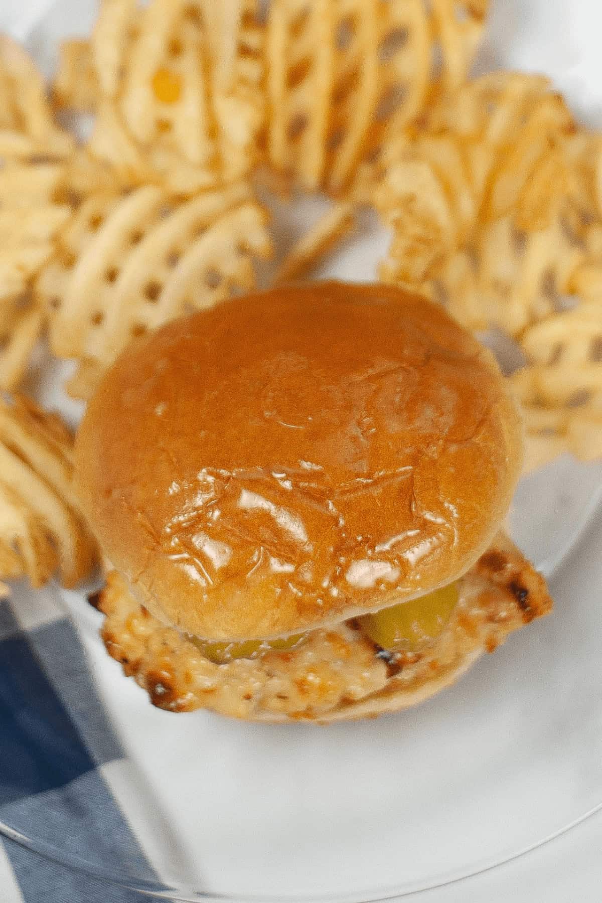 A roll with chicken on a plate surrounded by waffle fries.