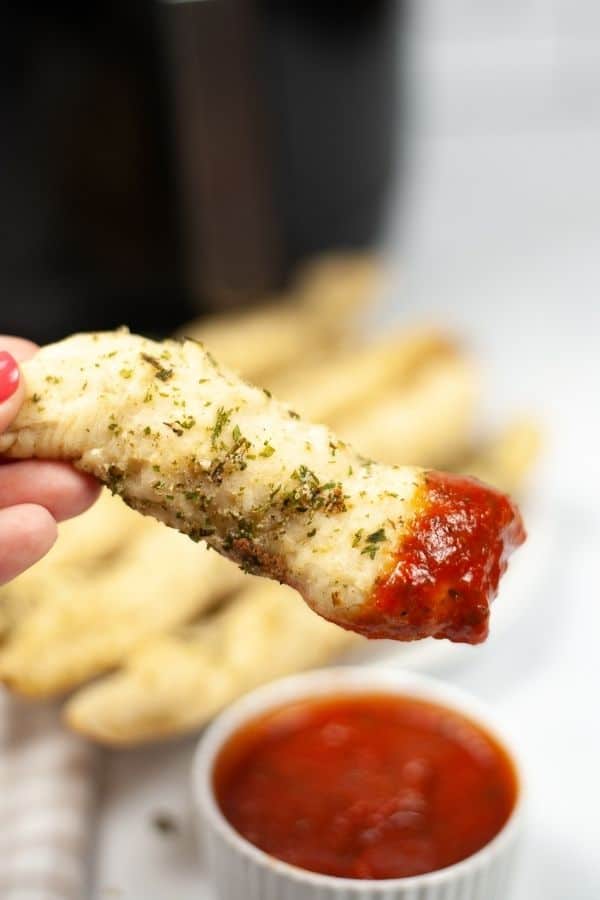 Hand holding a air fryer garlic breadstick dipped in sauce
