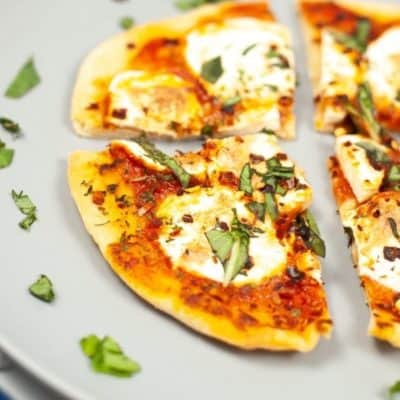 Cut up pizza on a plate with fresh herbs surrounding it